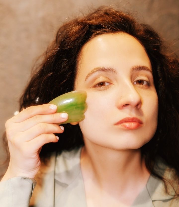 photo of woman using jade stone massager on her cheek